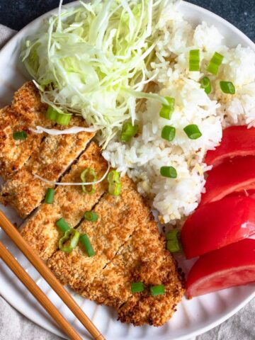 Plate of Air Fryer Katsu with sliced tomatoes, white rice and cabbage served on it.