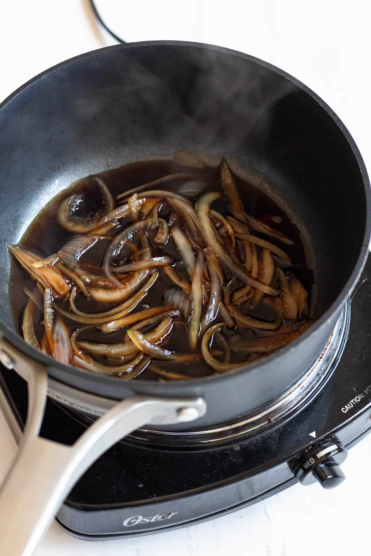 Saucepan with onions cooked to translucent in a brown sauce. 