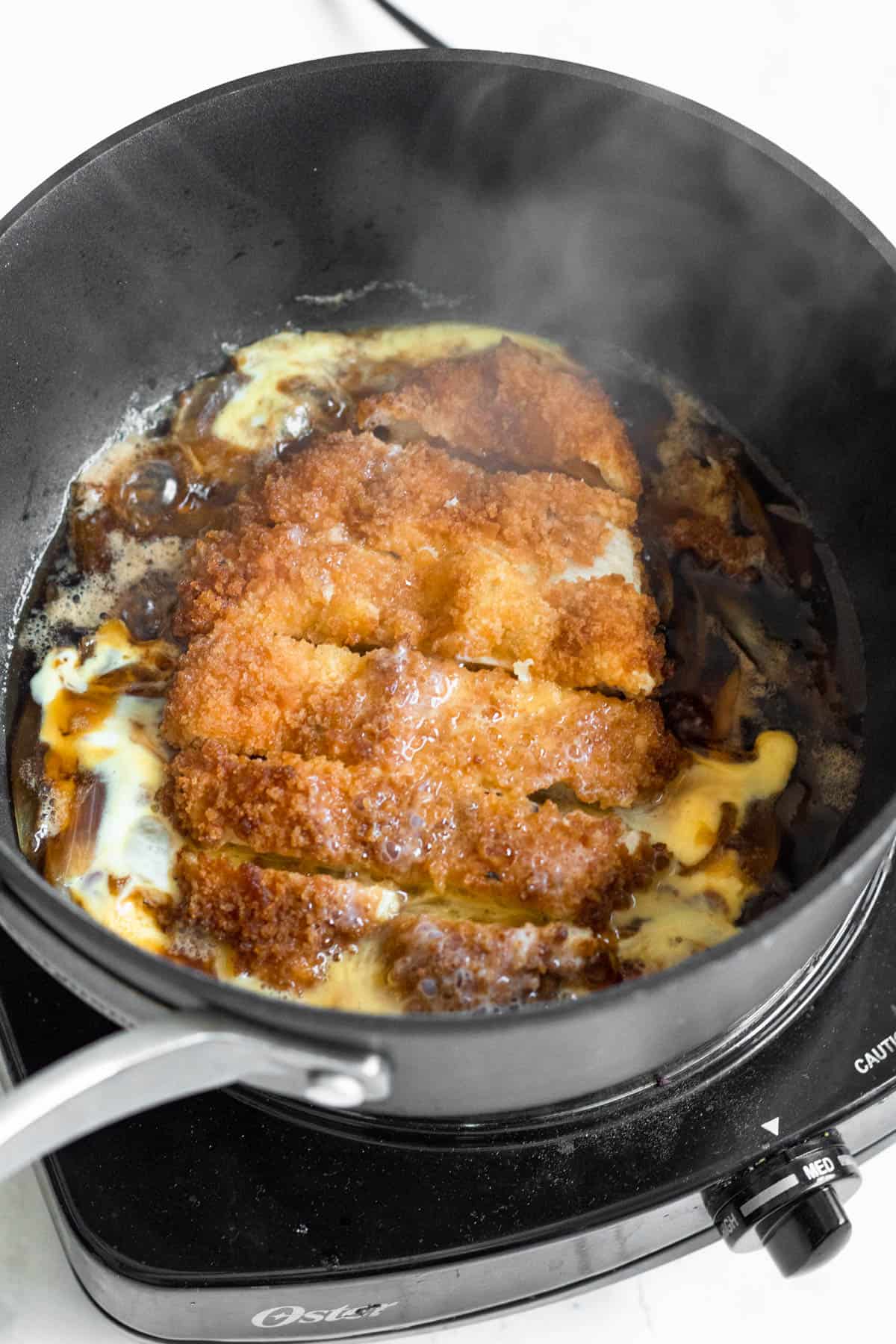 Chicken katsu and a beaten egg added to the onion mixture in the saucepan. 