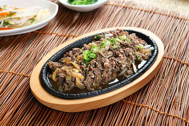 Korean style beef bulgogi served in an oval serving dish placed on a table with other dishes. 
