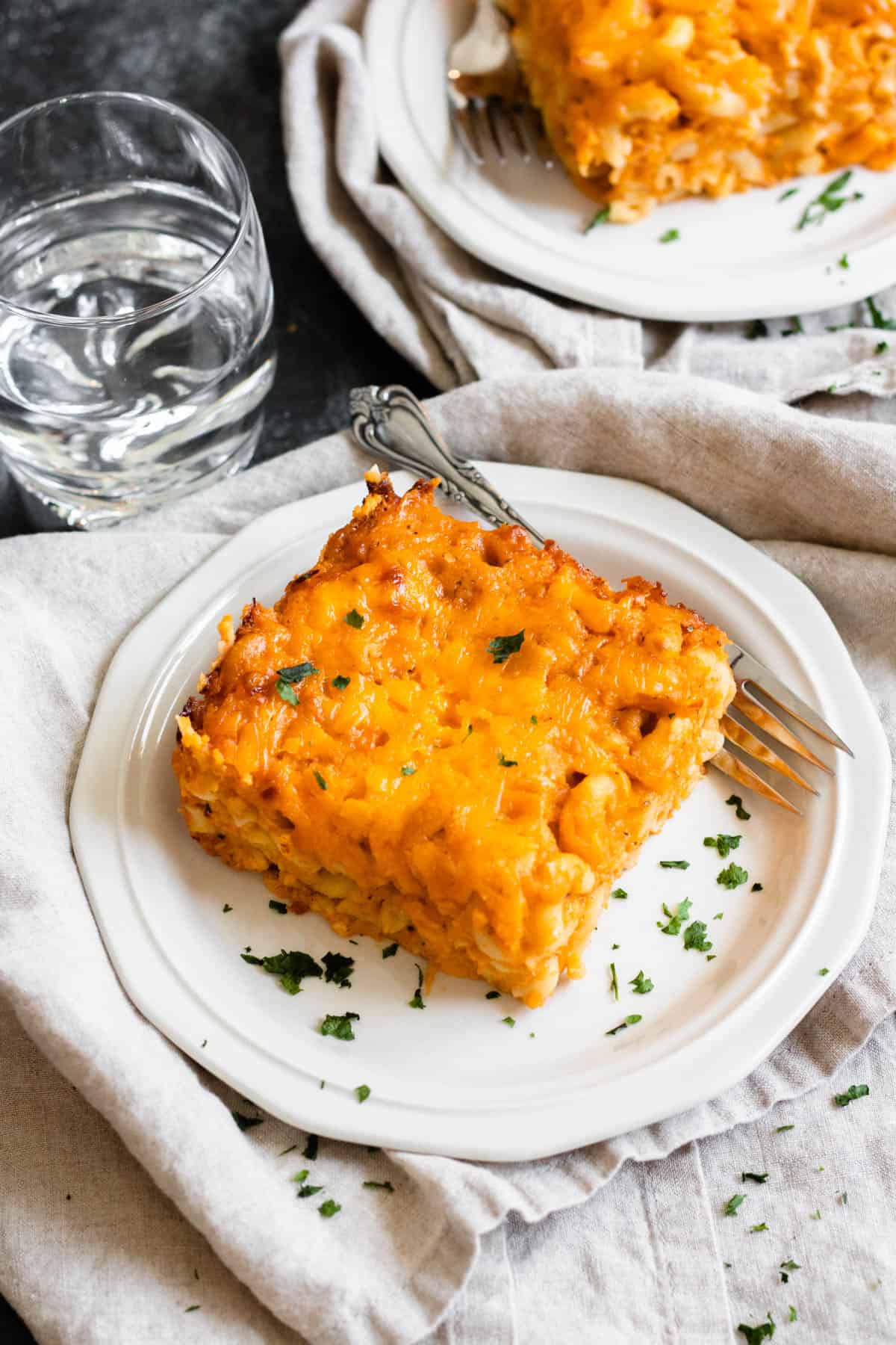 Slice of macaroni pie recipe on a plate with a fork resting on the plate. 