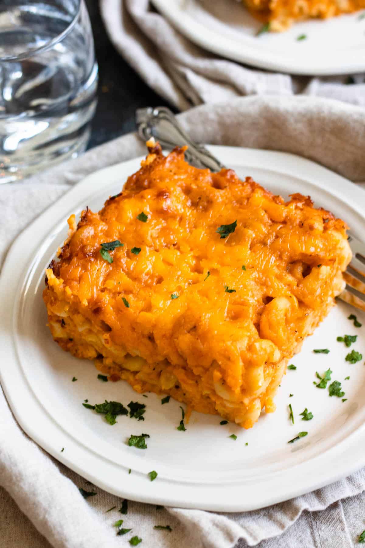 Large square piece of macaroni pie on a plate with a fork resting next to it. 