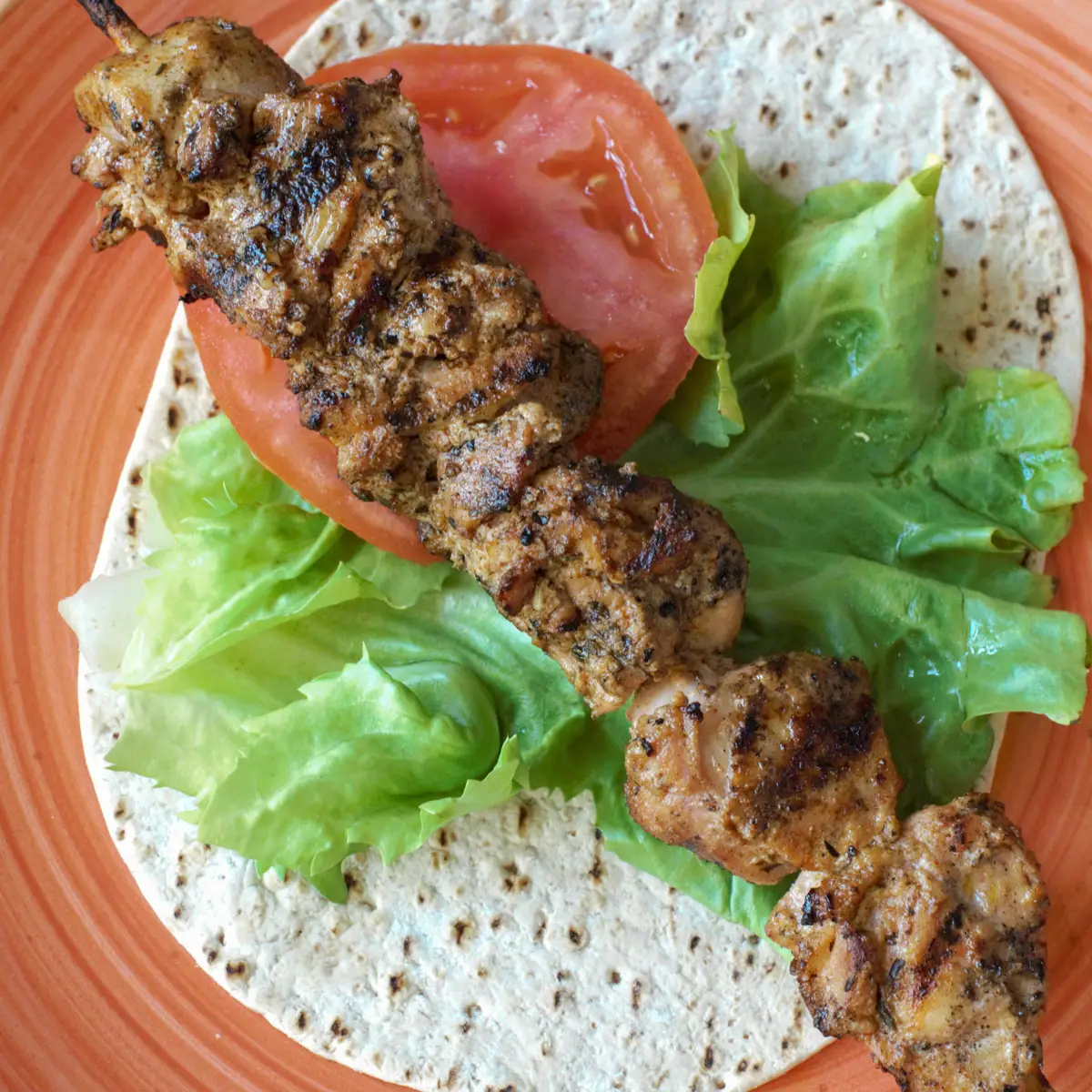 Greek Shish Taouk laying on a pita, with lettuce and tomato. 