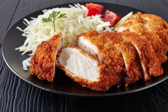 Tonkatsu sliced and served with tomato slices and cabbage on a plate. 