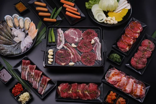 Platters of different types of raw beef surrounding a tabletop grill. 