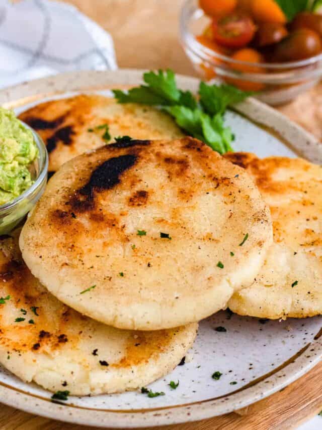 Arepas served on a plate with a small bowl of guacamole. 