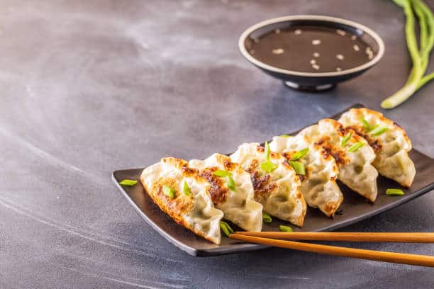 Gyoza dumplings served on a rectangular plate garnished with sliced green onions. 