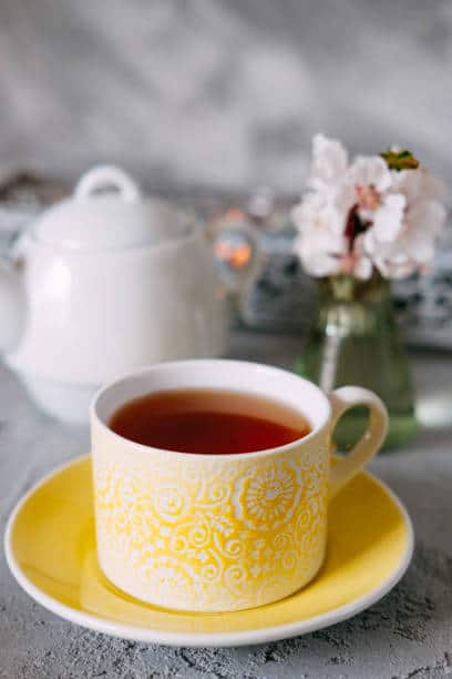 Golden colored breakfast tea on a saucer with a tea pot next to the cup. 