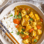 Pinterest image of a top view of a bowl with white rice and Japanese curry added to the side of it, with chopsticks resting on the side of the bowl.
