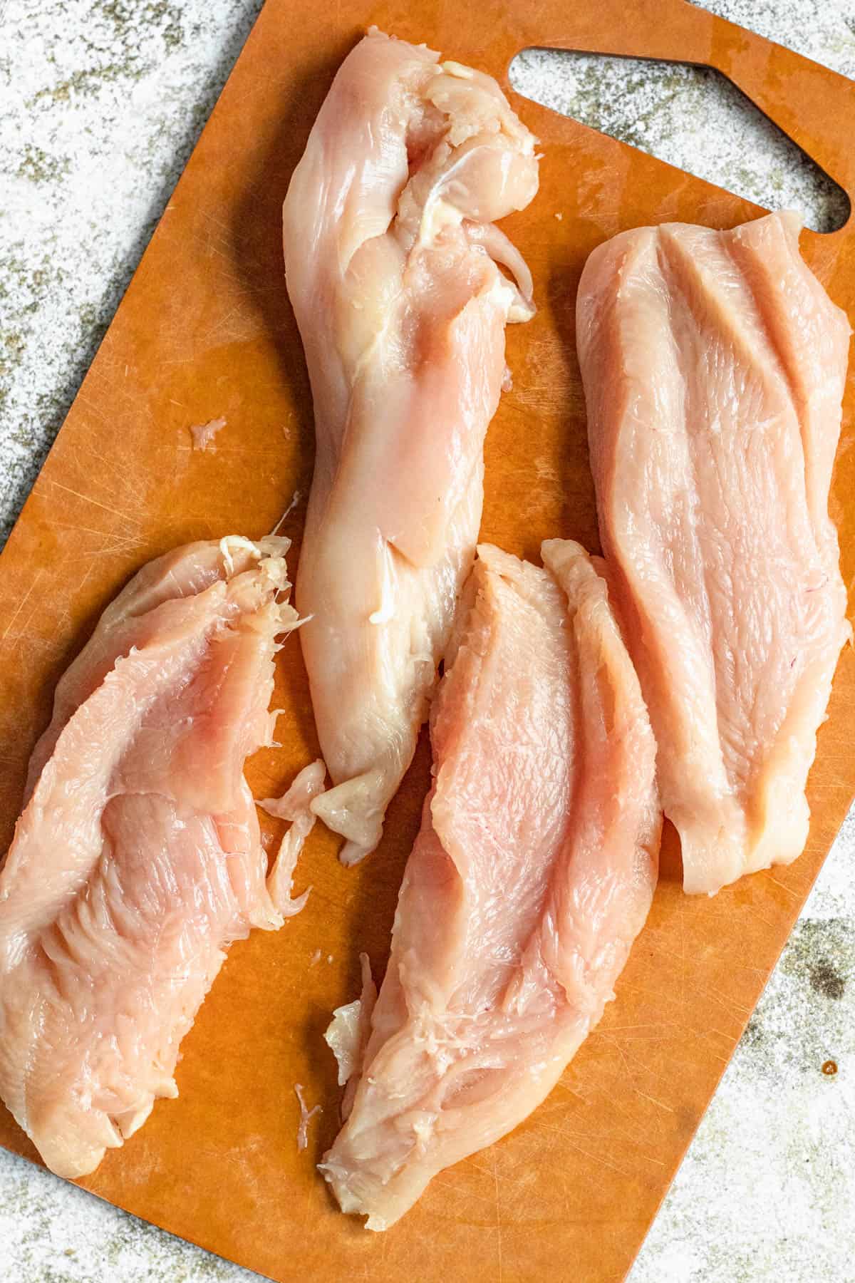 Chicken breasts sliced in half on a cutting board. 