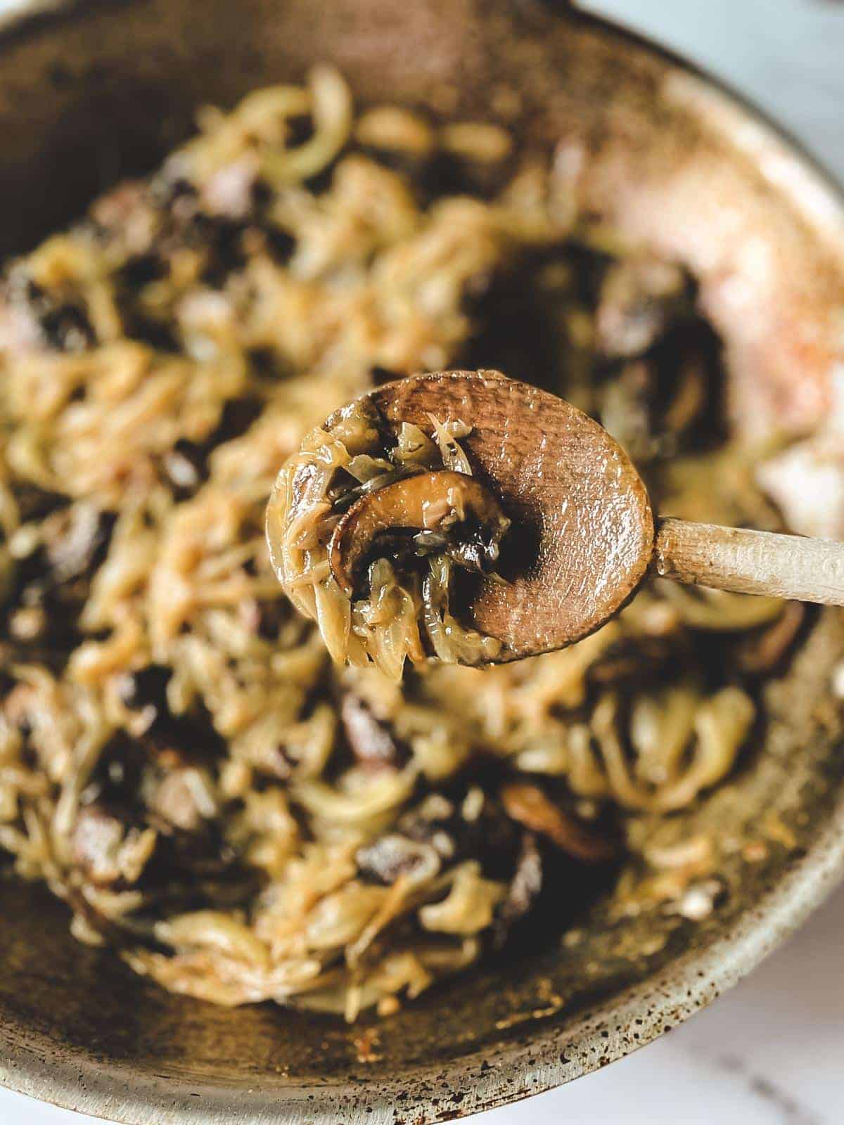Wooden serving spoon holding up caramelized onions and mushrooms.