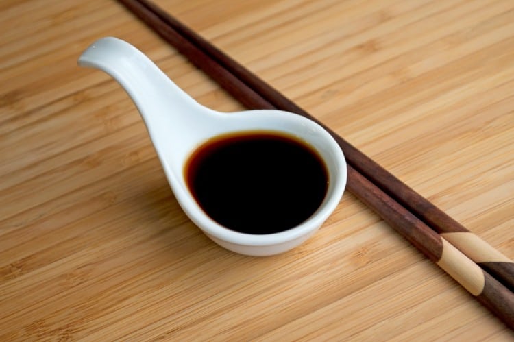 A small japanese ladle of coconut aminos with chopsticks resting beside it. 