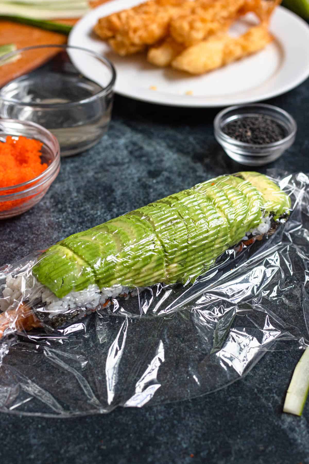 Plastic wrap covering avocado side of dragon roll sushi recipe. 