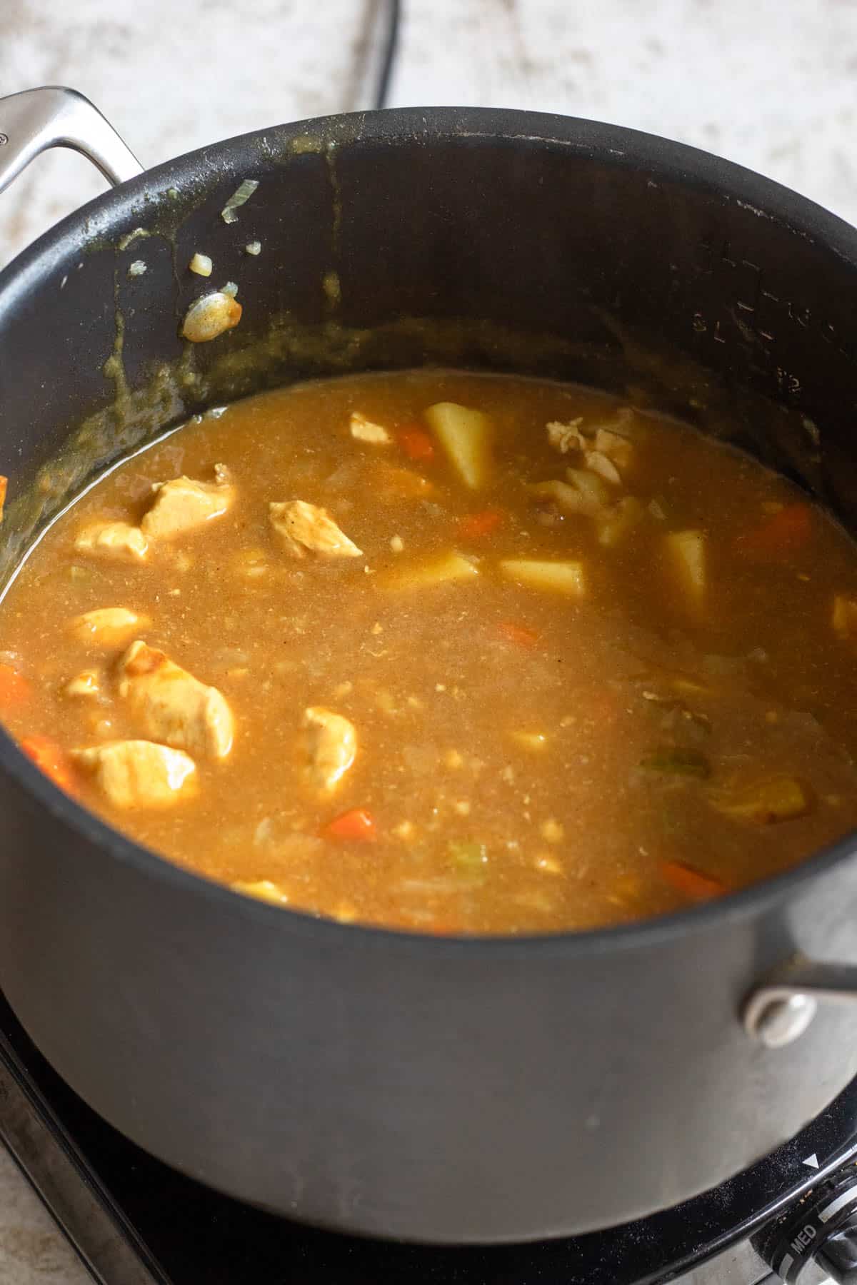 Golden curry seasoning mixed into the chicken mixture in a saucepan. 