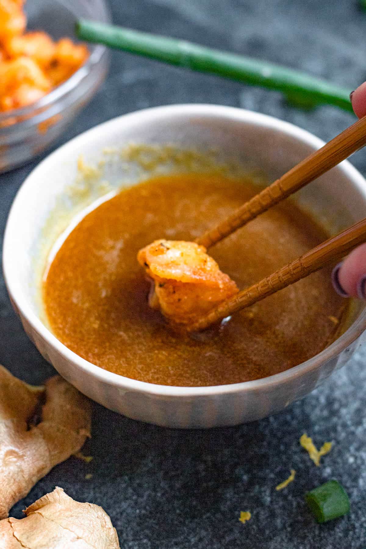 Ginger sauce in a bowl with chopsticks dipping a piece of shrimp into the sauce. 