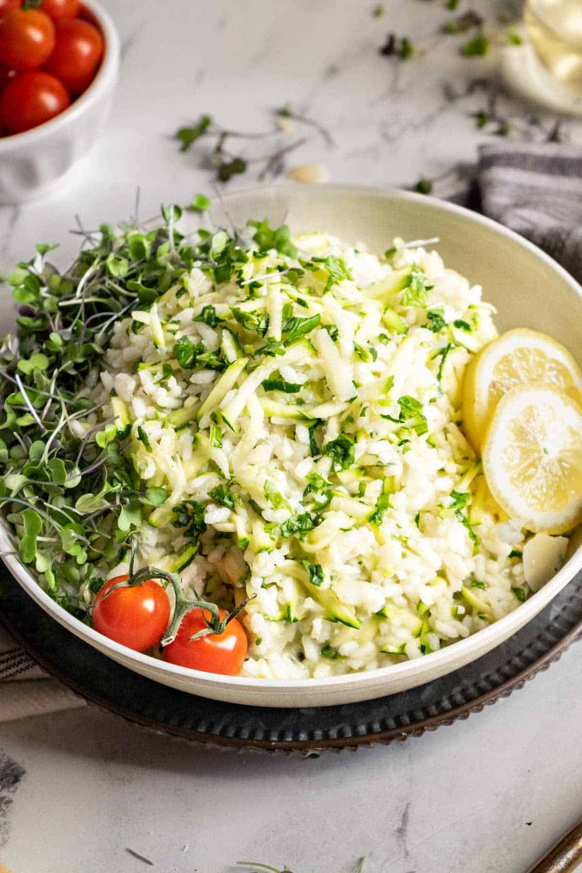 Zucchini Risotto in a bowl with lemon slices, tomatoes, and microgreens.