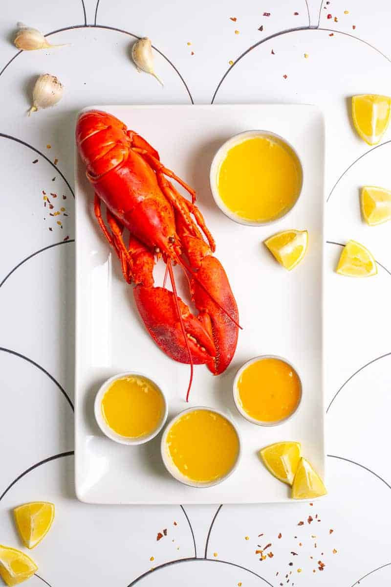 Lobster next to Butter Sauce and lemon wedges.