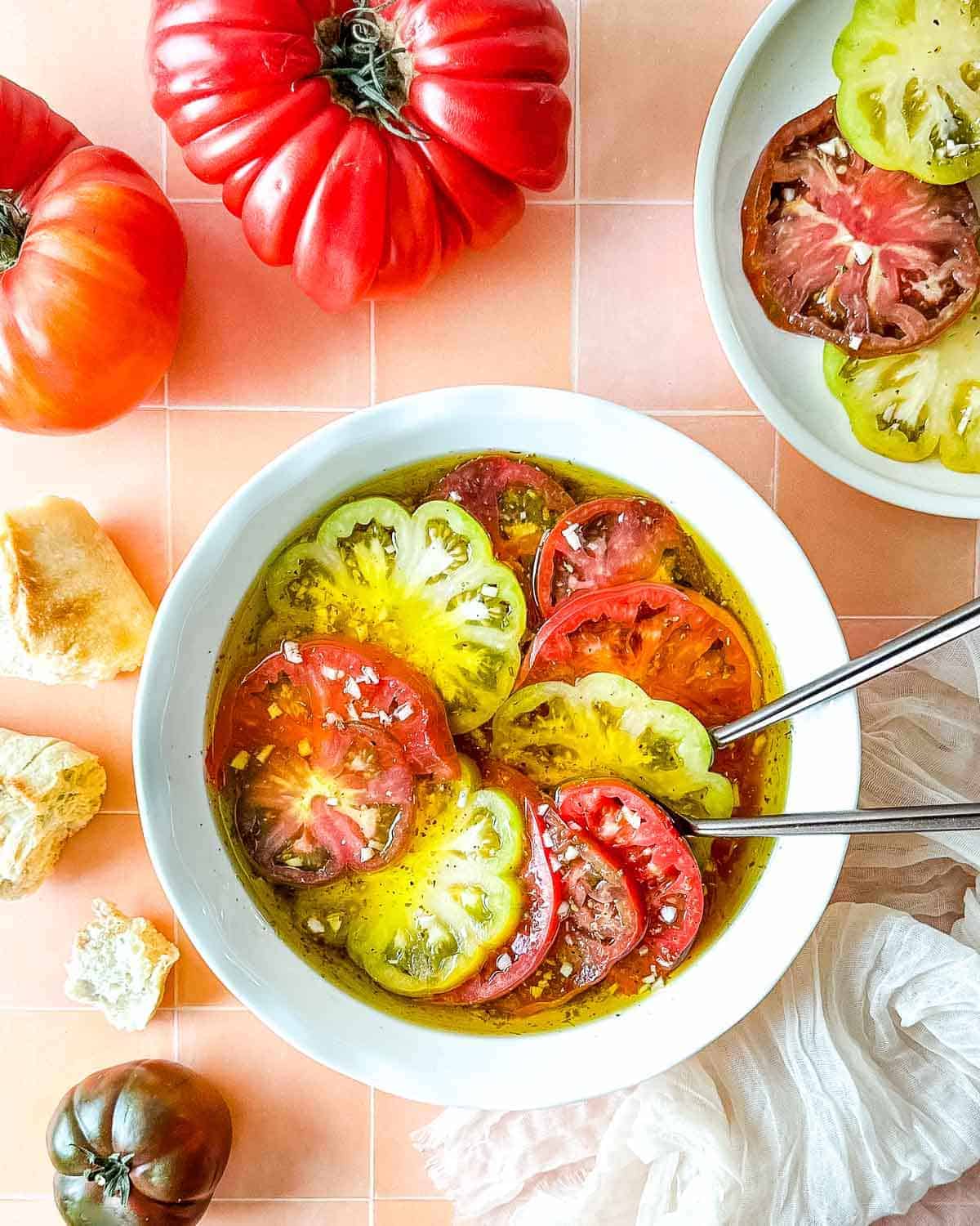 Marinated Heirloom Tomatoes in a shallow bowl with heirloom tomatoes around them. 
