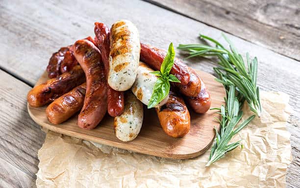 Wooden cutting board topped with several variety of German sausages. 