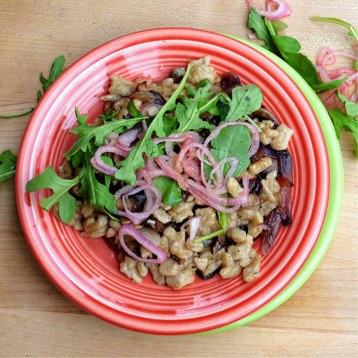 Rye sourdough Spaetzle on a plate with greens and cooked red onions garnished over it. 