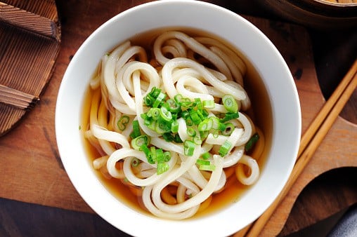 Udon noodles in broth in a bowl and garnished with green onions on top. 