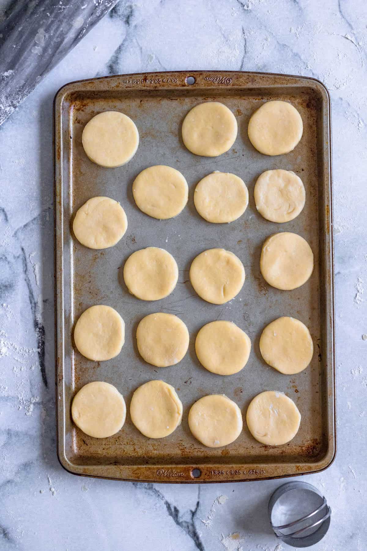 Alfajores cookie dough cut into circles are added to a baking sheet. 
