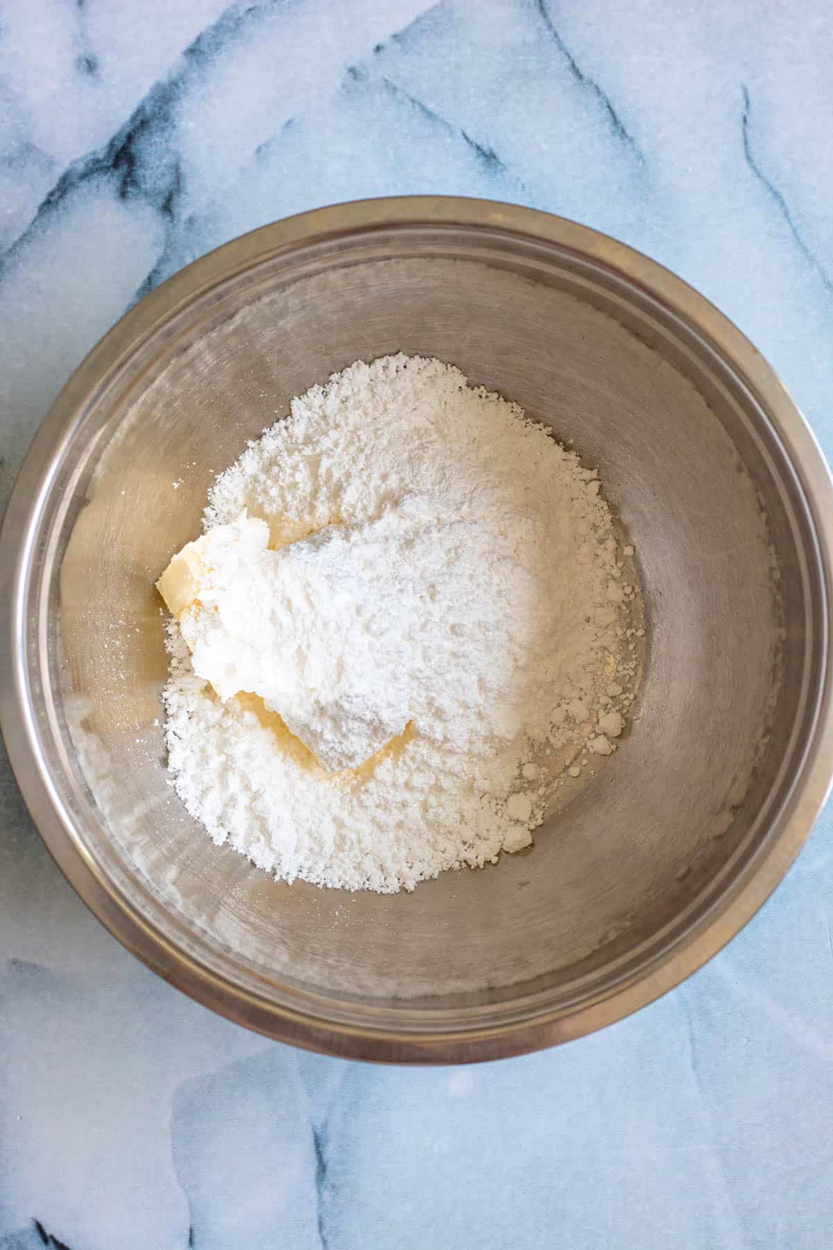 Butter and powdered sugar added to a mixing bowl to prepare alfajores. 