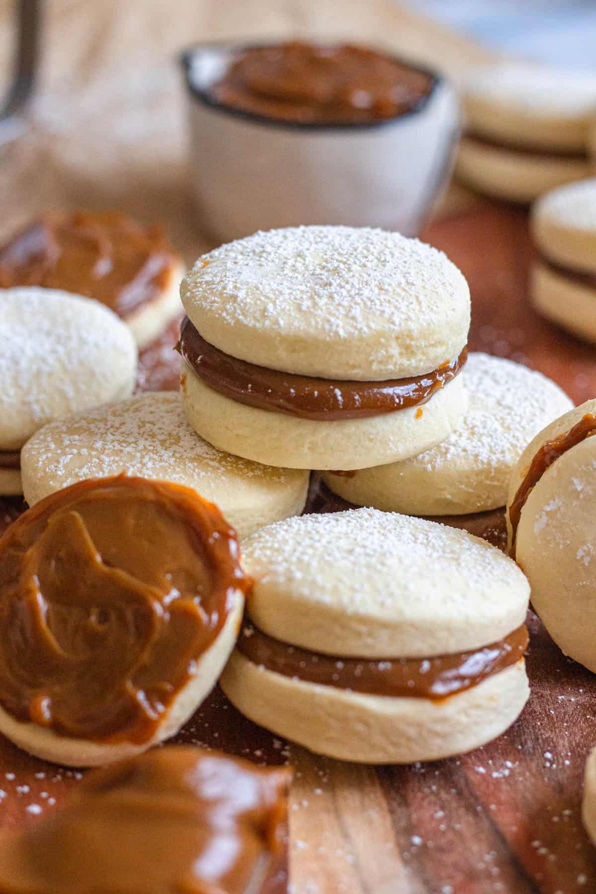 Alfajores Argentinos laying stacked and next to each other, with one filled with dulce de leche but not sandwiched with another cookie. 