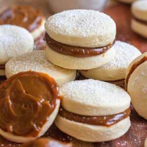 Alfajores shortbread sandwich cookies on a tray with one cookie opened to reveal the creamy mixture.