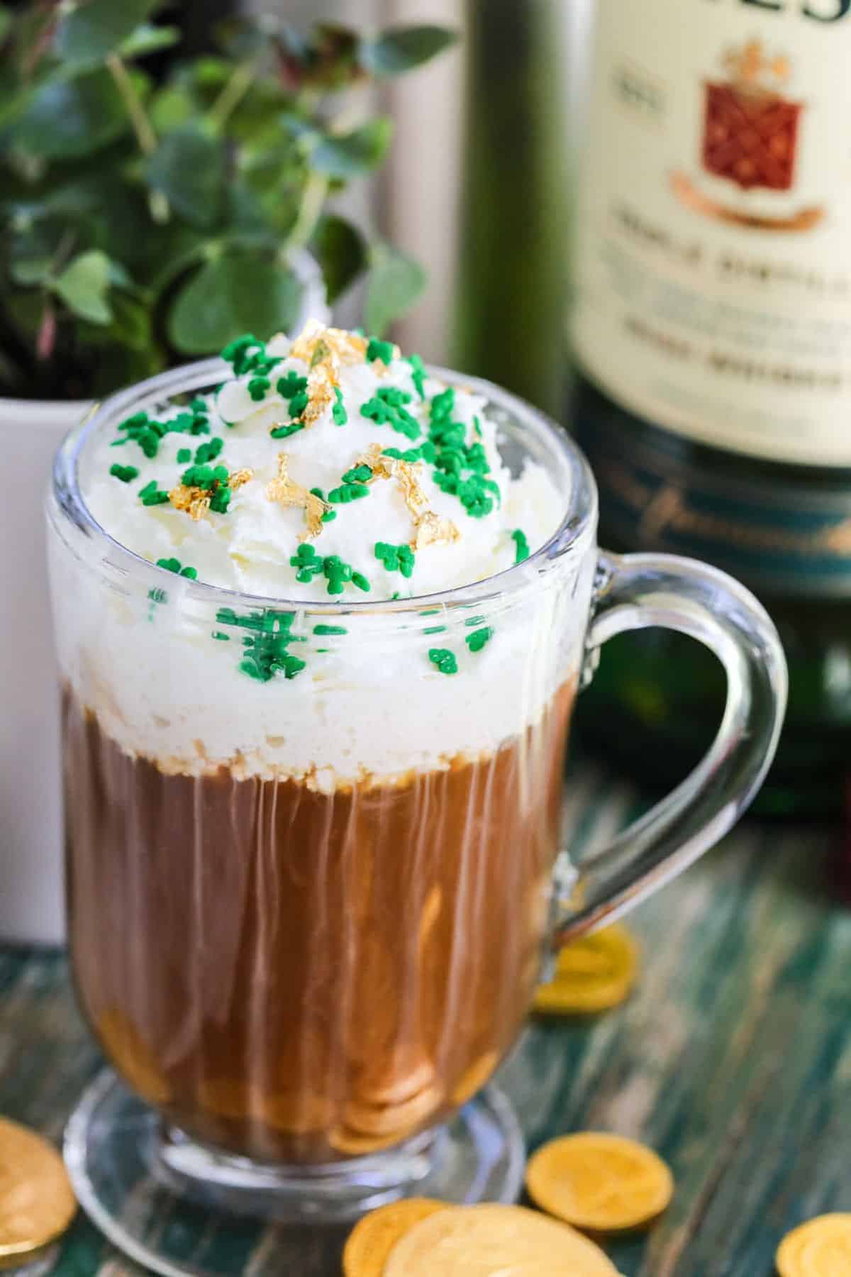 Irish coffee in a glass coffee mug topped with whipped cream and green sprinkles on top. 
