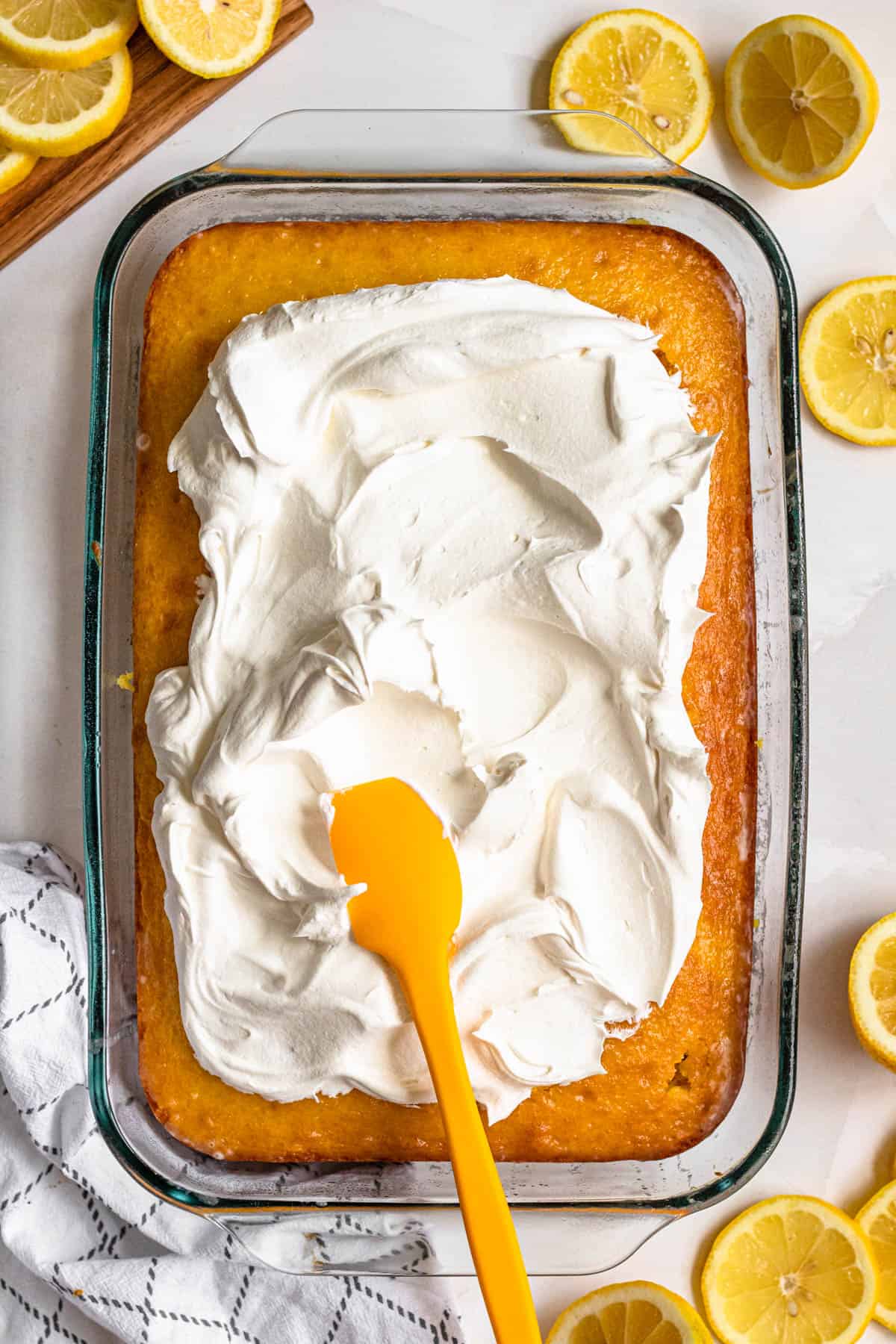 Lemon cake recipe with whipped topping being spread over the baked lemon cake. 