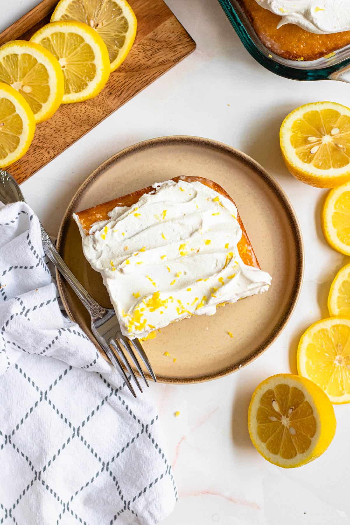 Top view of a slice of lemon cake with cool whip on top and fresh lemon zest over the top and a fork resting on the side. 