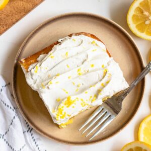 Lemon cake on a small plate topped with lemon zest and cool whip.
