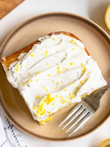 Lemon cake on a small plate topped with lemon zest and cool whip.