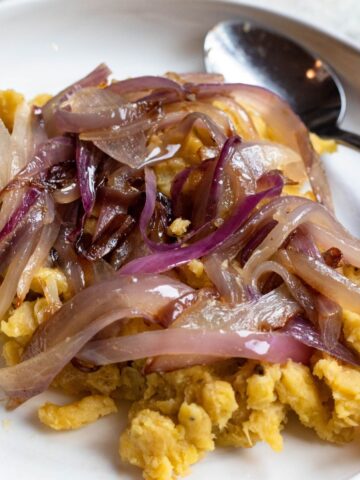 A plate of mangu with red onions on top.