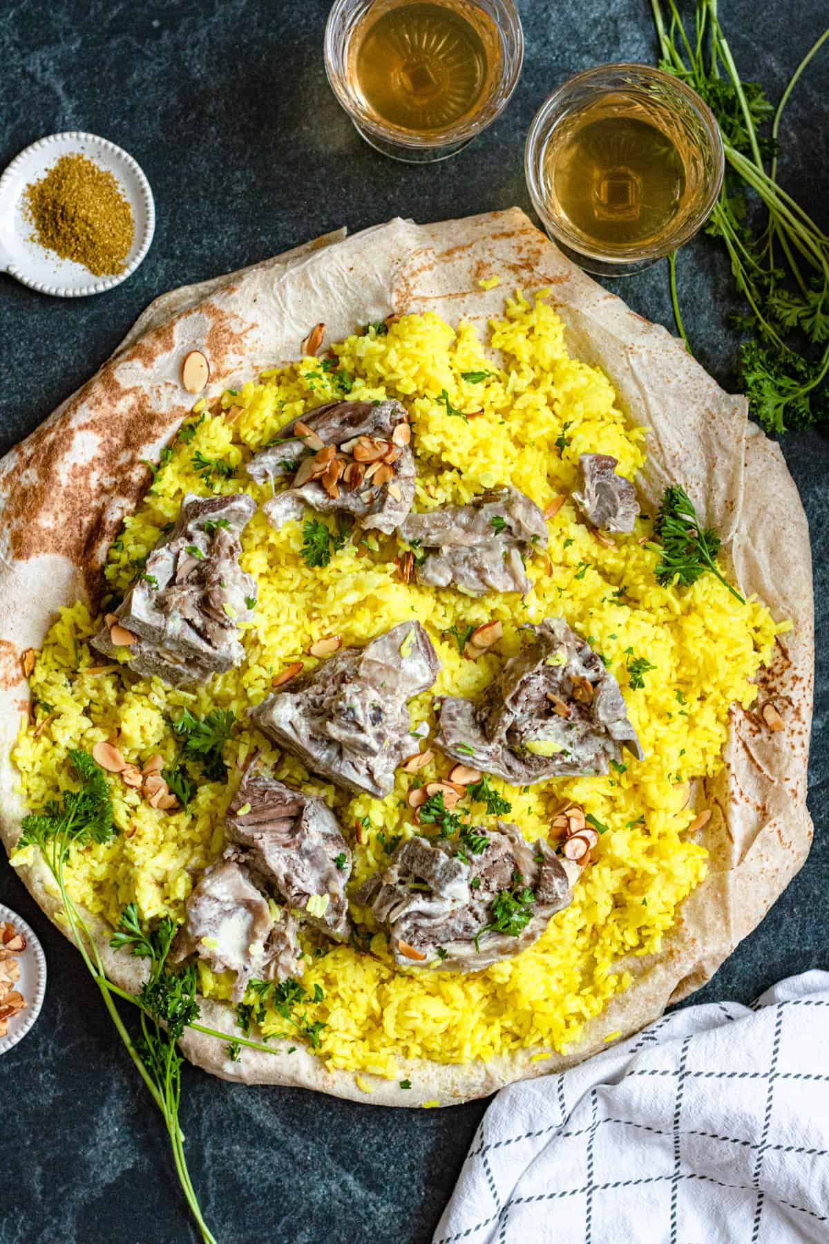 Top view of mansaf served over saj with tender lamb, toasted almonds and parsley over the seasoned rice. 
