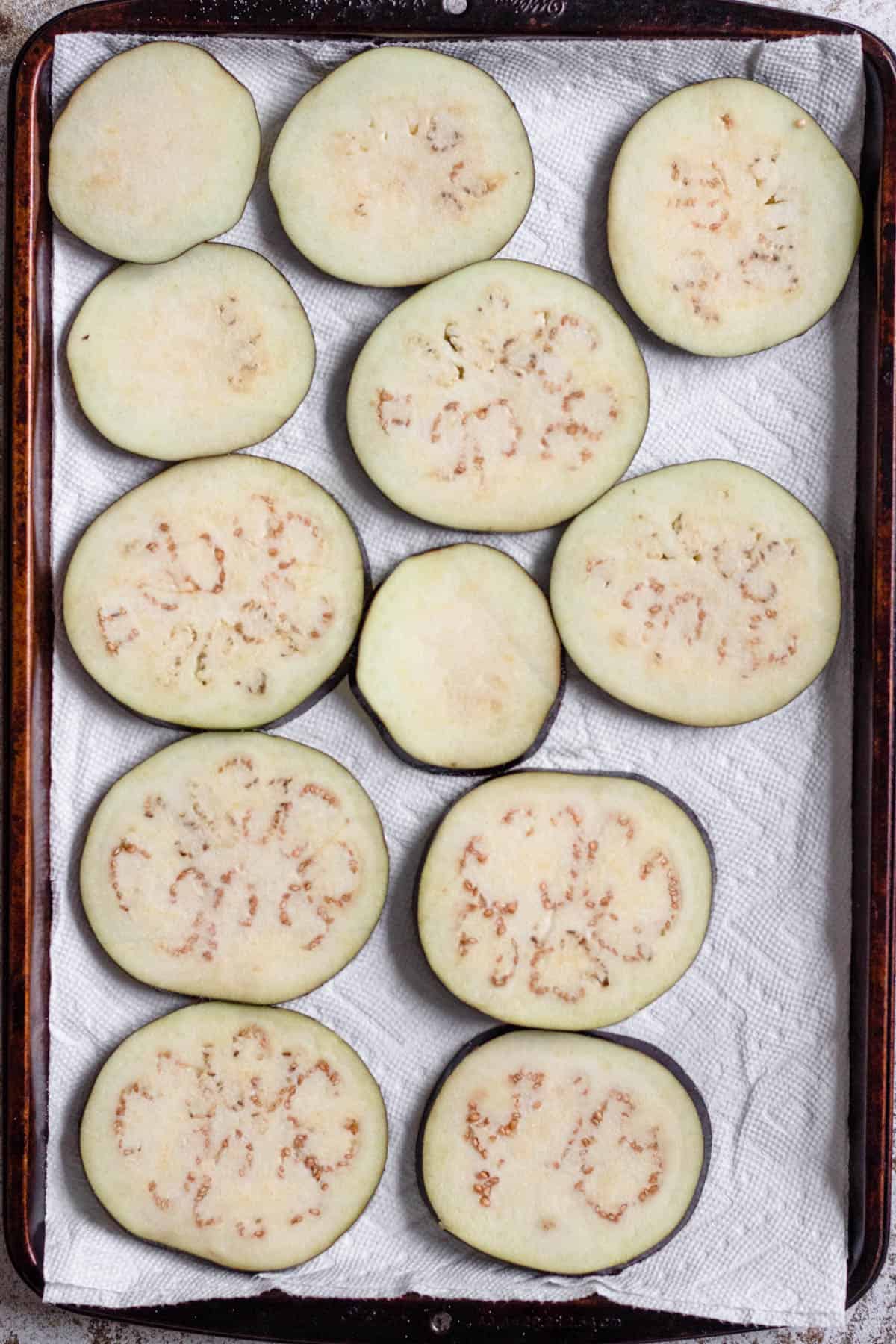 Eggplant rounds sliced and laid on top of a paper towel and topped with salt. 