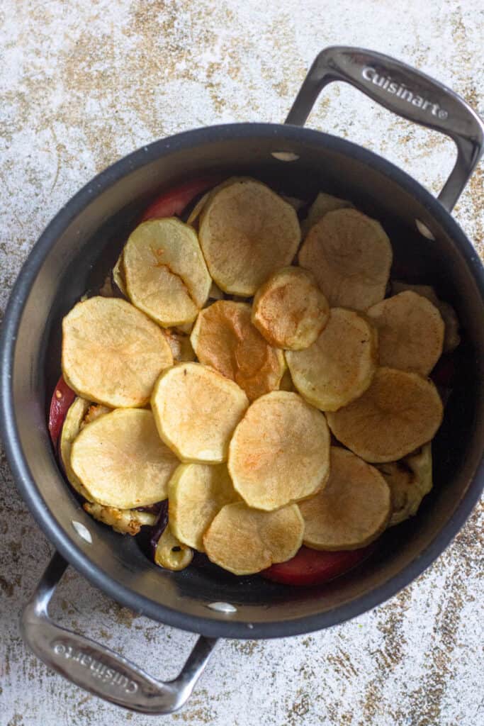 Tomatoes and fried potato rounds layered into a dutch oven to begin assembling maqluba.