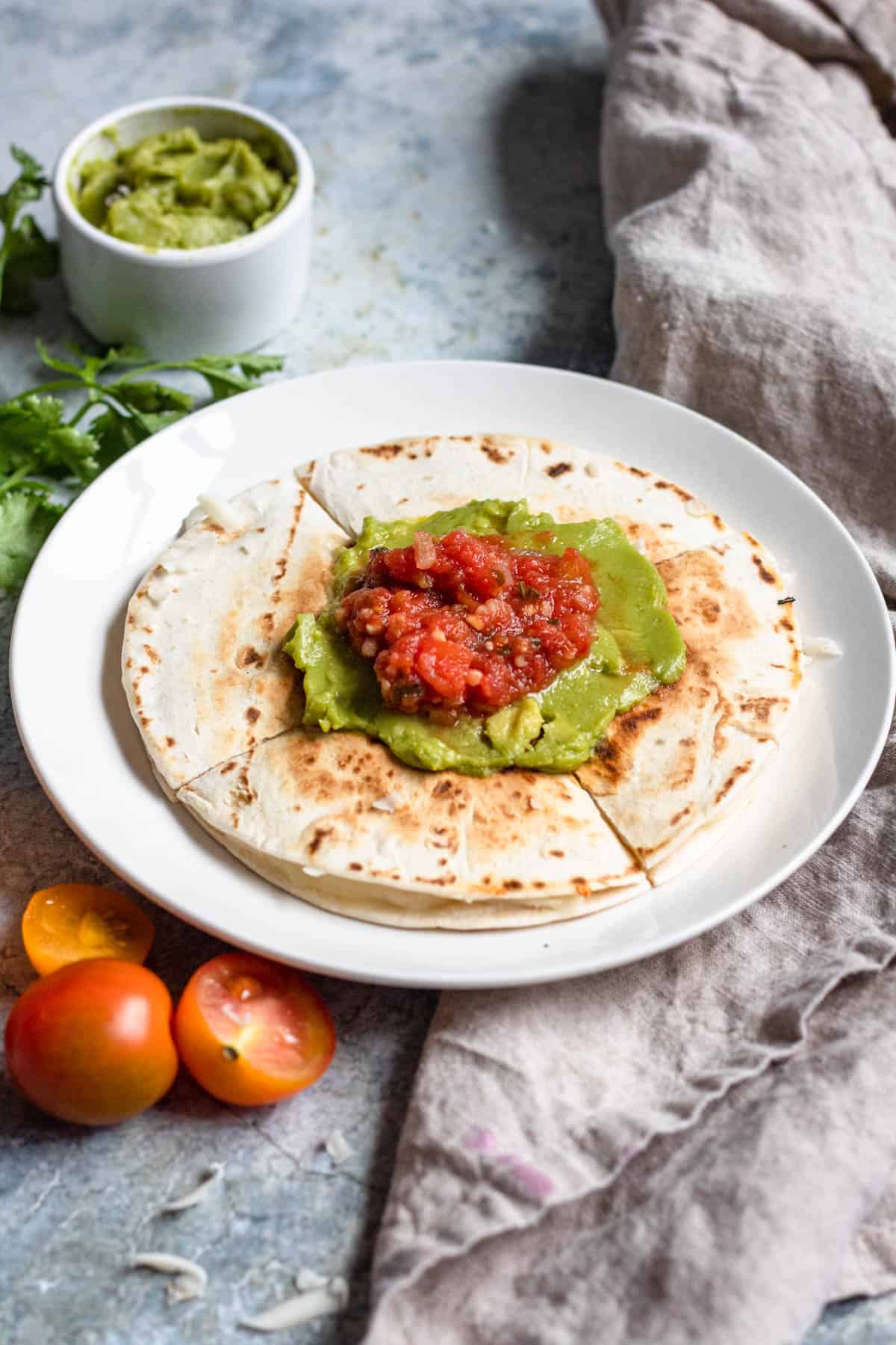 Sincronizadas cut into fours and topped with guacamole and salsa with cherry tomatoes laying next to the plate. 