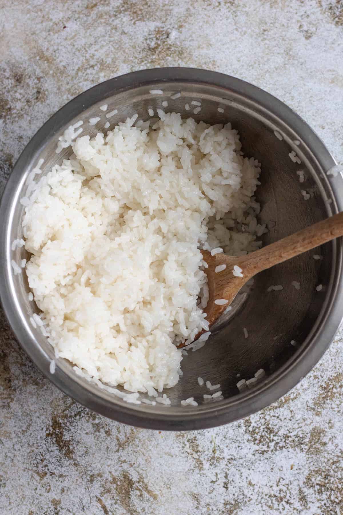 Wooden spoon stirring sugar mixture into the cooked Japanese rice. 