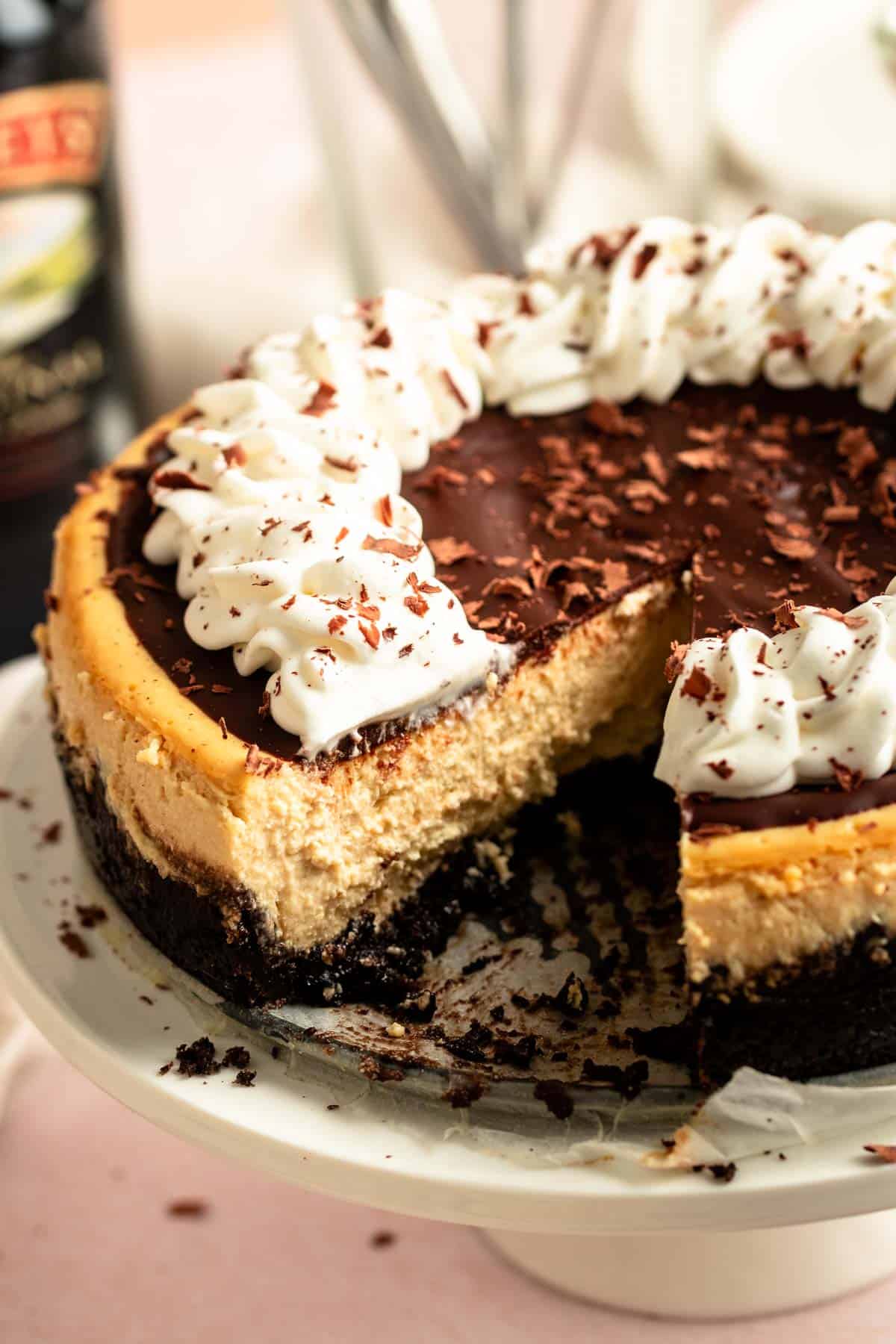 Baileys irish cheesecake with whipped cream on top and chocolate shavings over the top served on a cake stand. 
