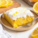 Pinterest image of a slice of lemon cake on a small plate with a fork resting on the side and lemon slices on a cutting board beside it.