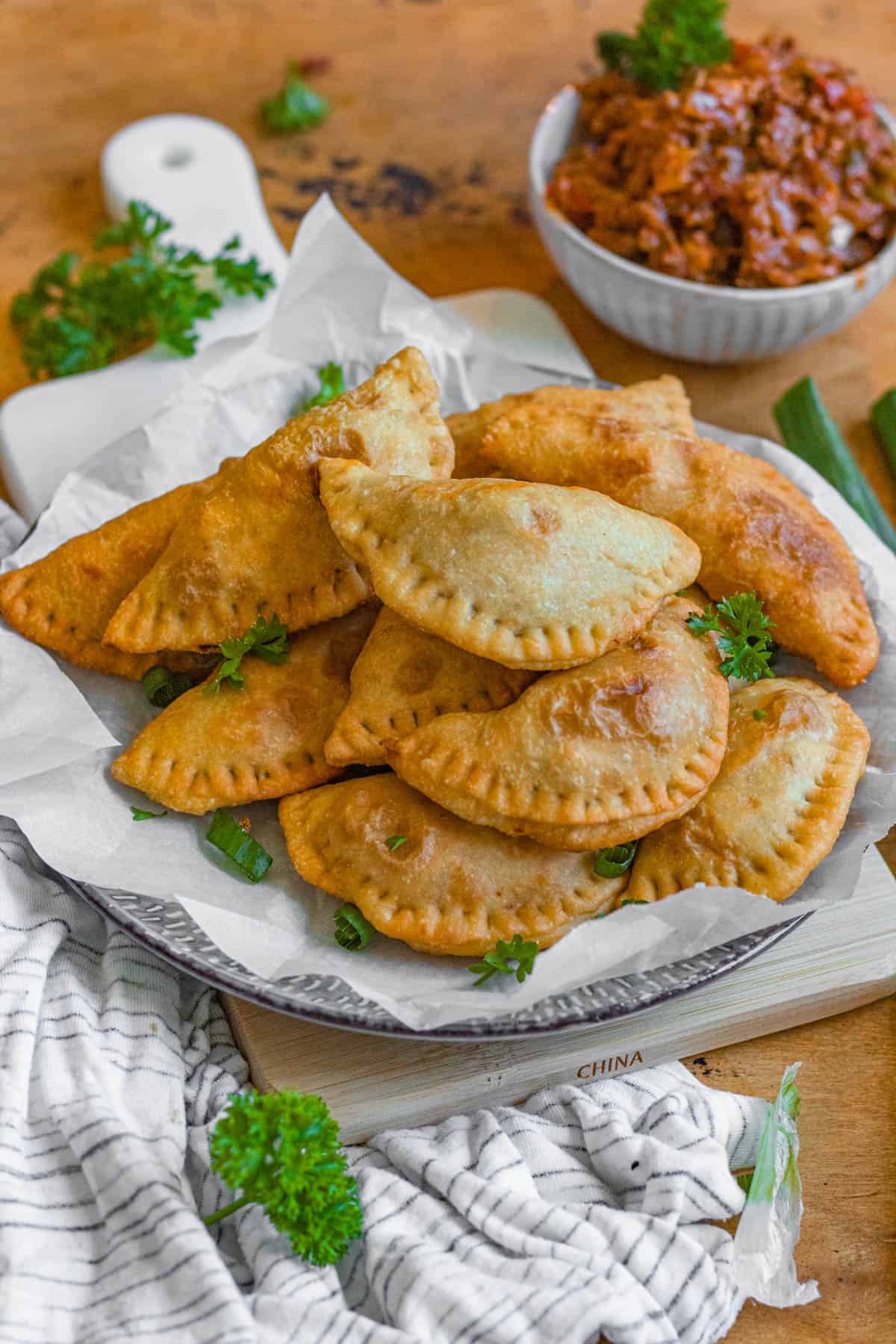Plate of golden brown fried beef empanadas with a small bowl of ground beef filling beside it. 