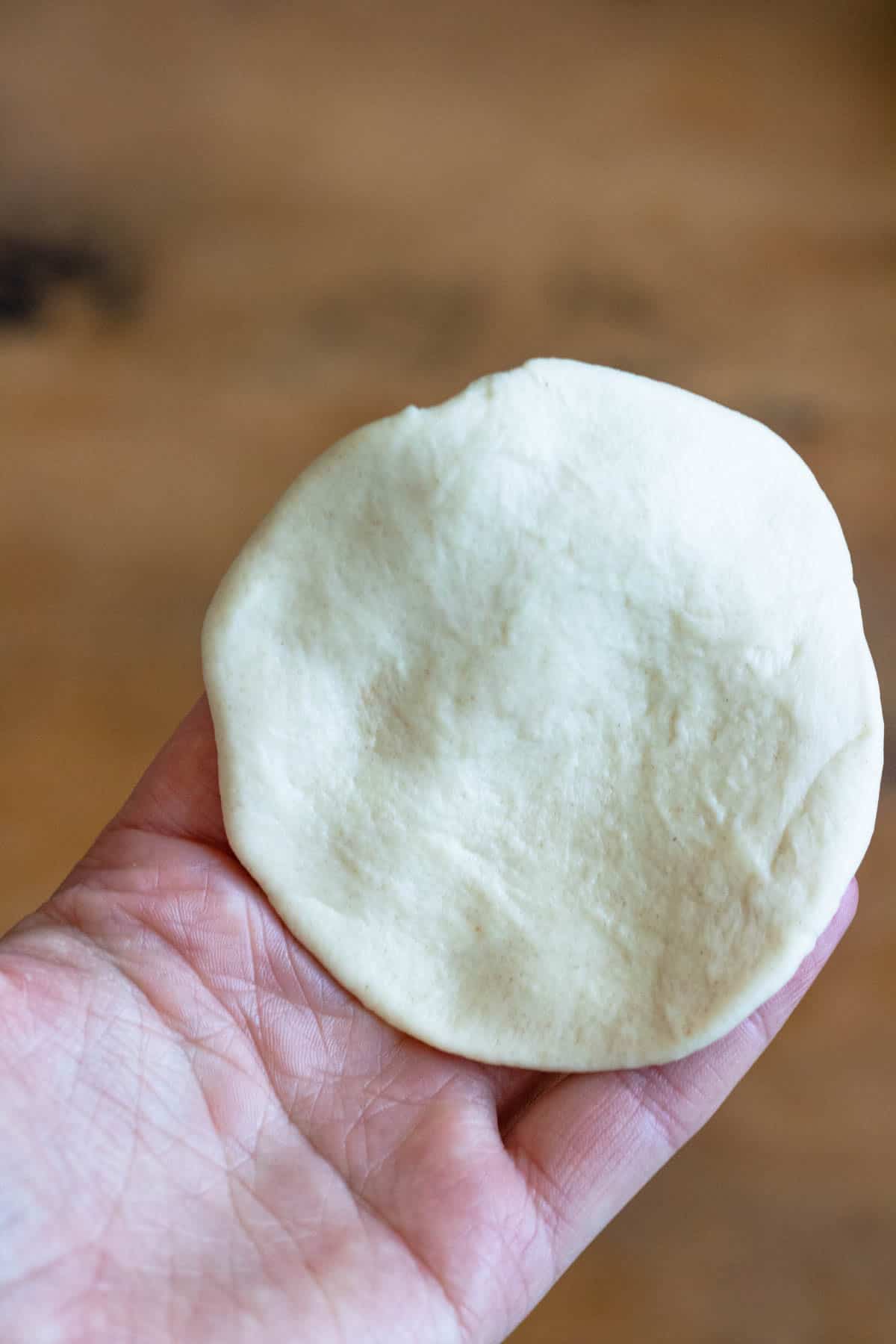 Hand holding a piece of dough for preparing beef empanada.