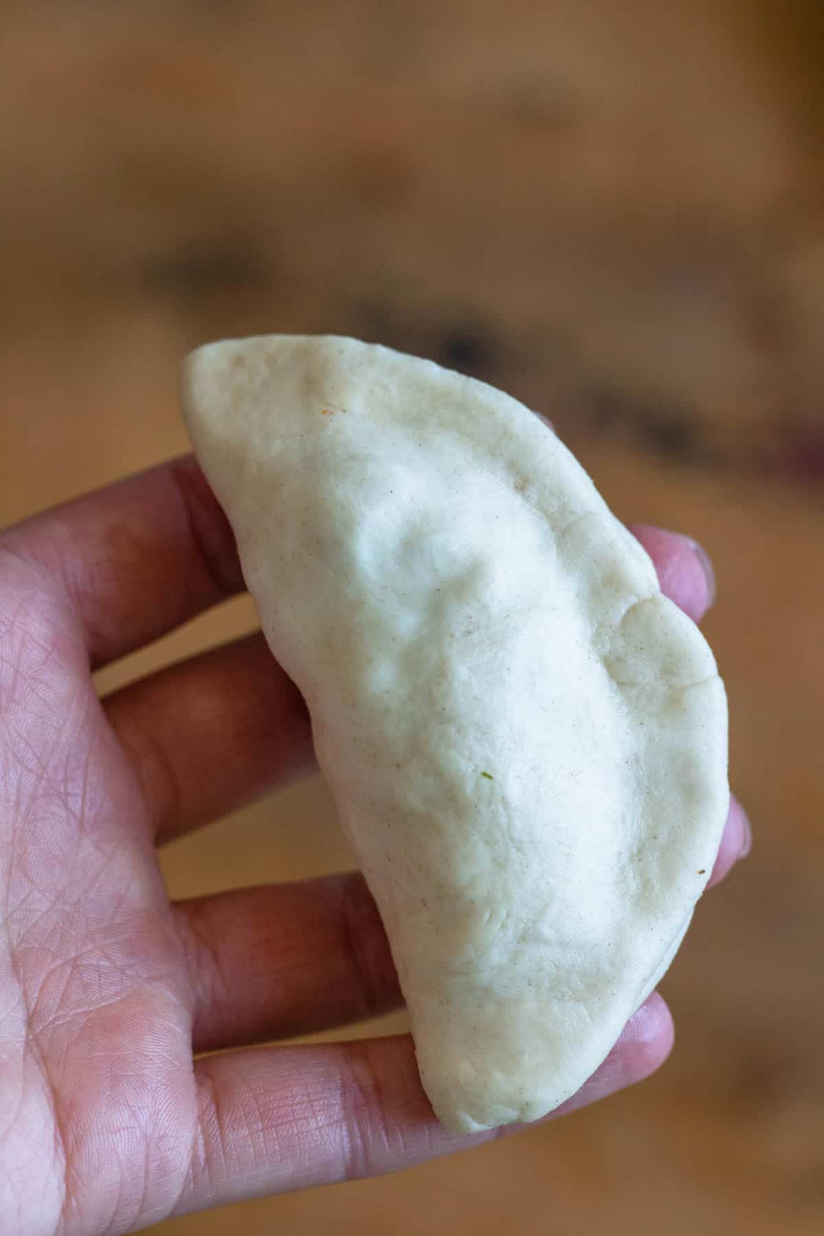 Hand holding up a stuffed  beef empanada ready to fry.  