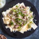 Beshbarmak on a platter with noodles, onions, and broth, topped with parsley.