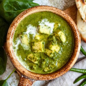 Palak paneer in a serving crock drizzled with cream.