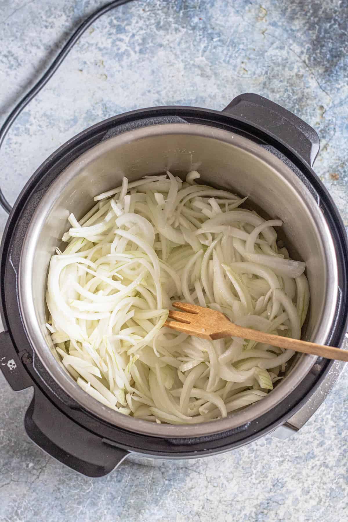 Raw sliced sweet onions inside an instant pot to make instant pot french onion soup. 