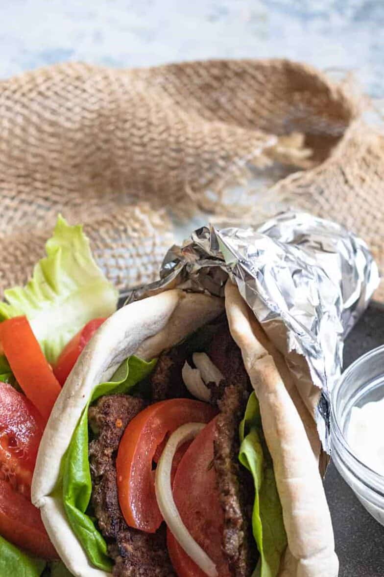 A gyro wrapped in tinfoil, showing the meat, sliced tomatoes ad lettuce, ready to serve. 