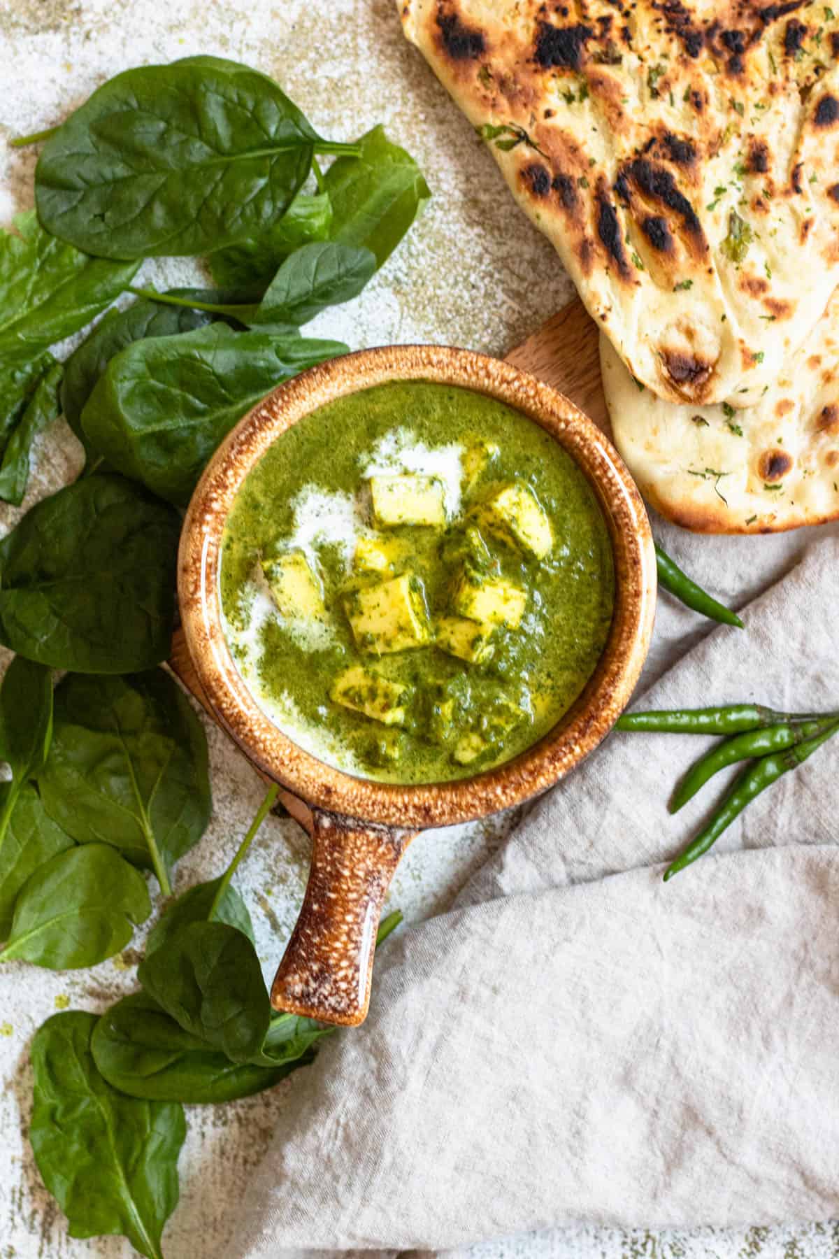 Naan bread laying next to a bowl of easy palak paneer in a crock. 